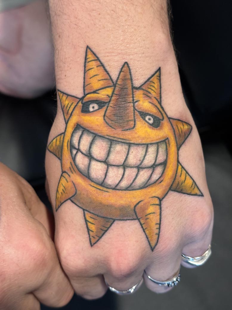 Colorful cartoon sun with a big toothy grin tattoo