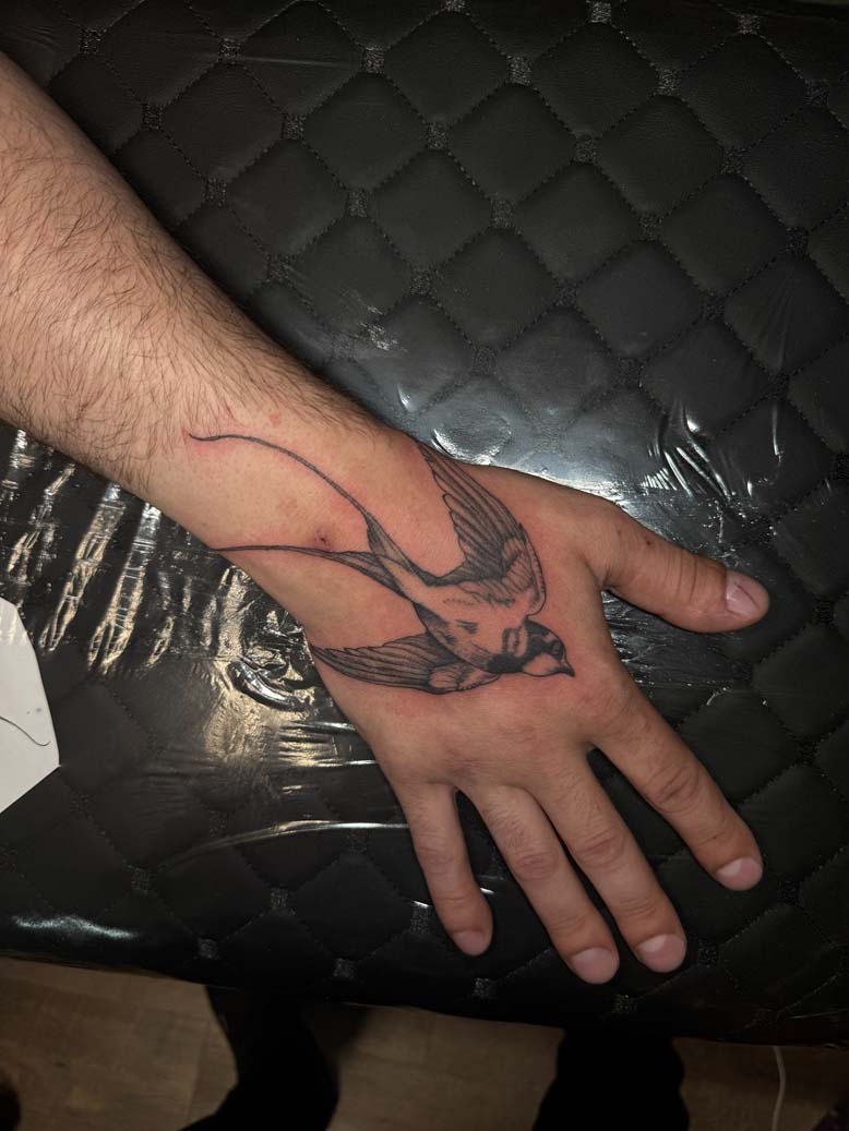 Black ink bird tattoo on the back of a hand