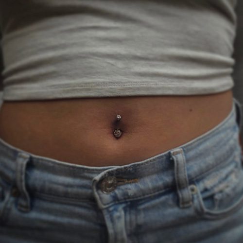 Woman wearing tee and jeans, showing new belly button piercing