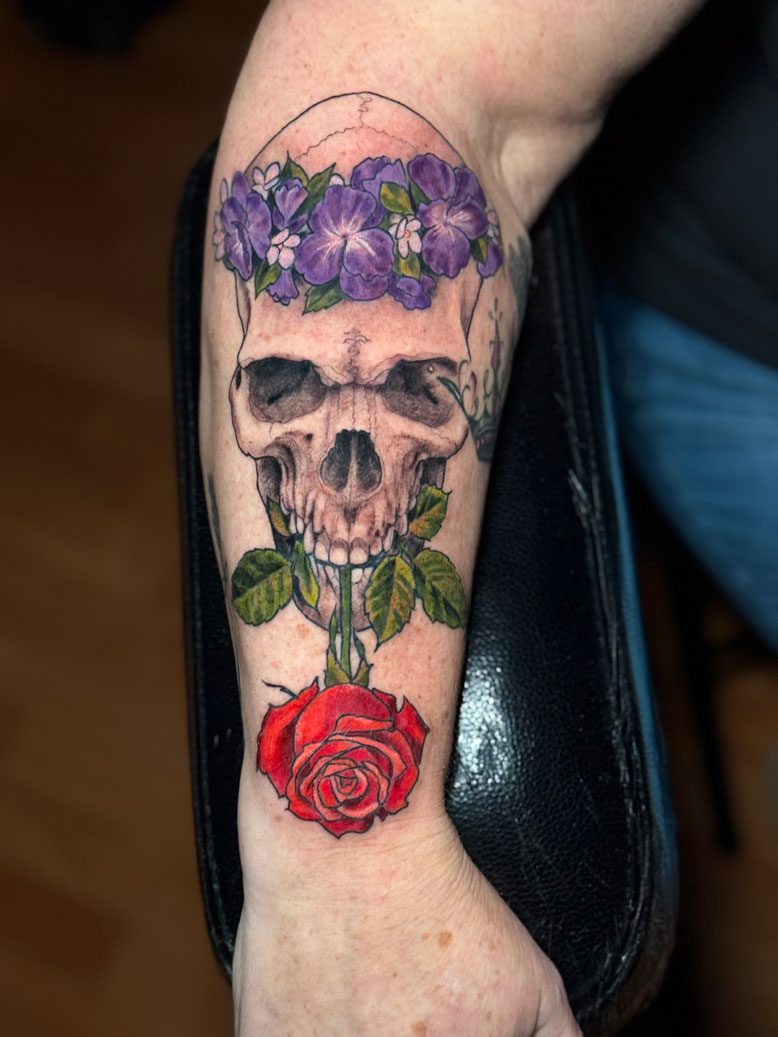 Skull with a crown of flowers biting a red rose
