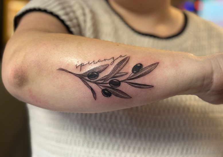 A forearm tattoo of a plant with the Italian word speranza